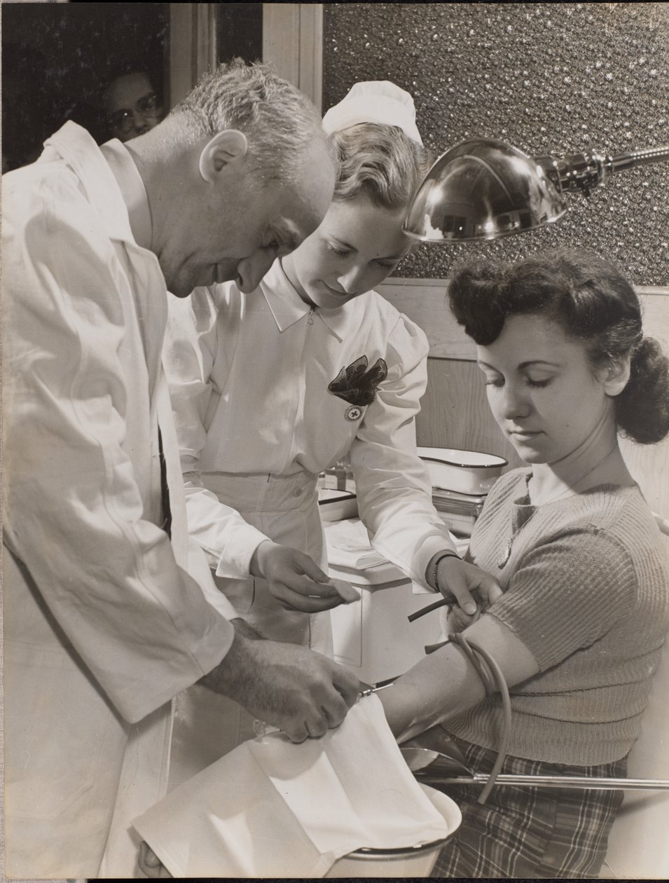 [Arzt und Krankenschwester setzen einer Frau eine Nadel ein] von Arnold Eagle