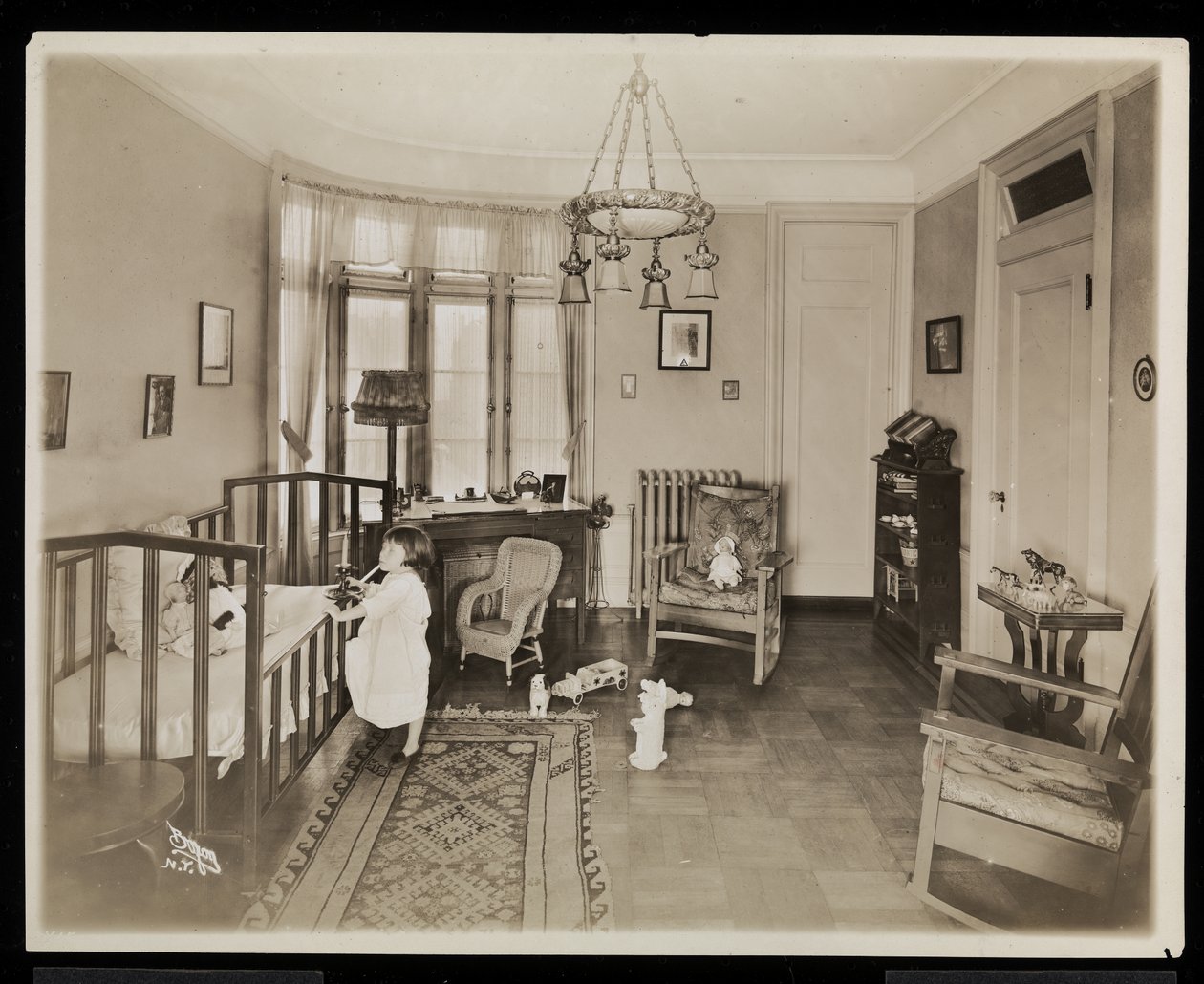 Ein Mädchen, das eine Kerze hält und in ein Kinderbett steigt, in einem Schlafzimmer der A.C. Cronin Residenz, 1915-16 von Byron Company