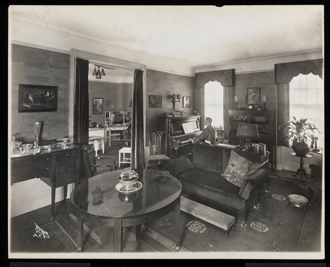 Ein Mann spielt Klavier in einem Wohnzimmer der A.C. Cronin Residenz, 1915-16 von Byron Company