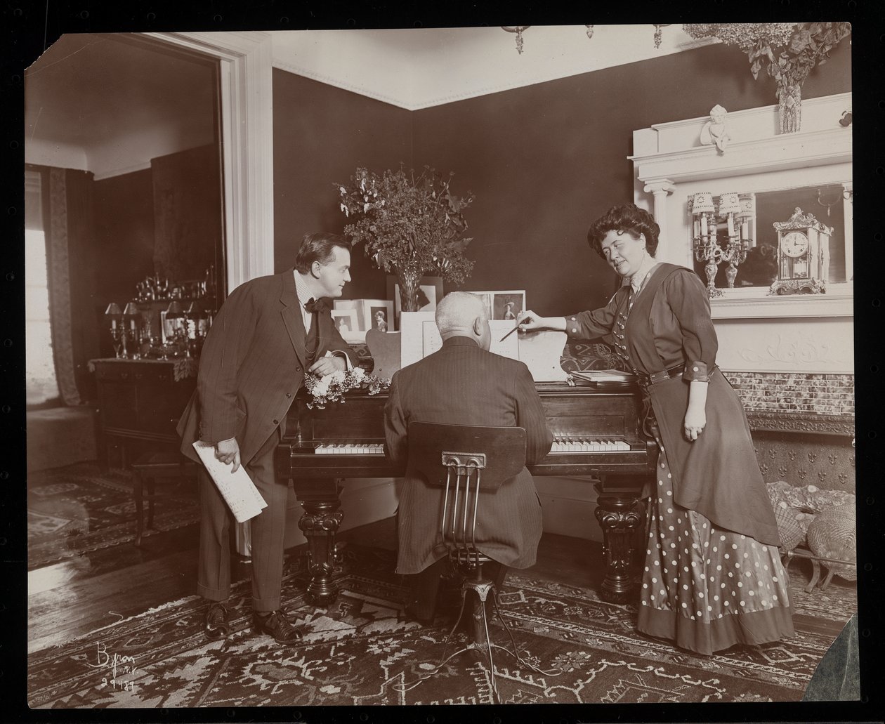 Clara De Regand zeigt auf eine Partitur, während ein Mann Klavier spielt, 1910 von Byron Company