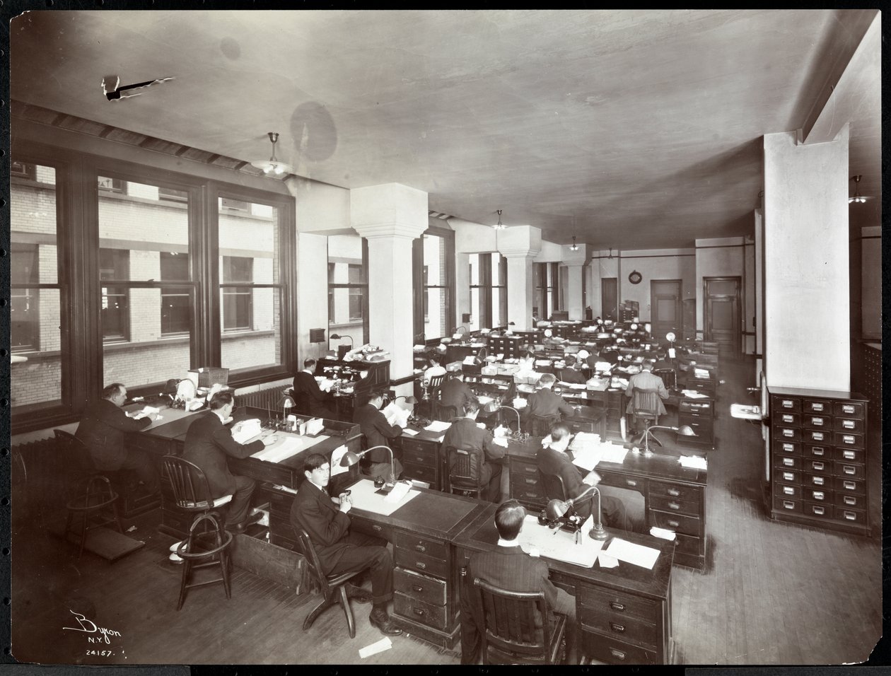 Männer und eine Frau arbeiten an Schreibtischen in einem Büro der Metropolitan Life Insurance Co. an der 23rd Street und Madison Avenue, New York, 1907 von Byron Company