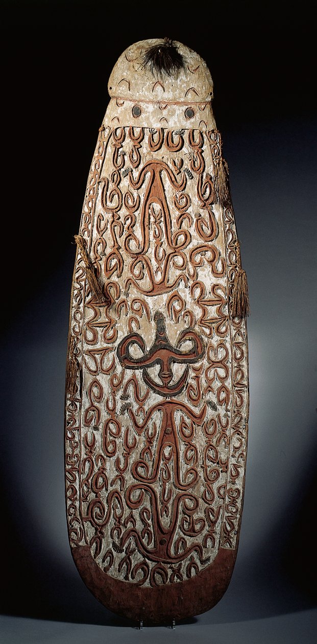 Ovaler Asmat-Schild, reliefartig geschnitzt mit scrollenden Ornamenten, die stark stilisierte Figuren einbeziehen, geflochtene Quasten am Rand von Guinean New