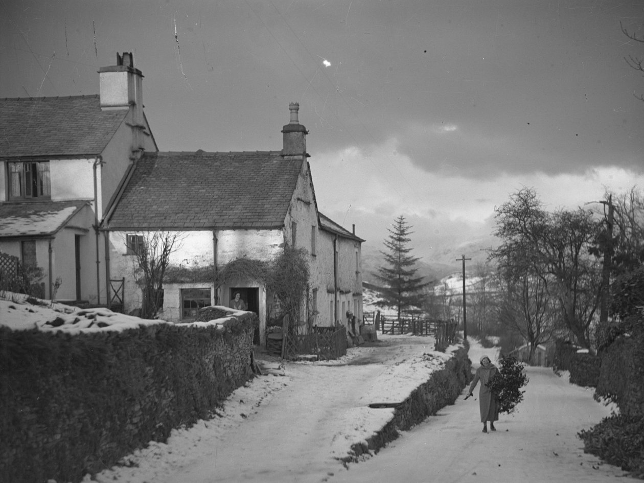 Frau trägt Ast auf Straße neben Borwick Fold Farm in Hawkshead im Schnee von Joseph Hardman