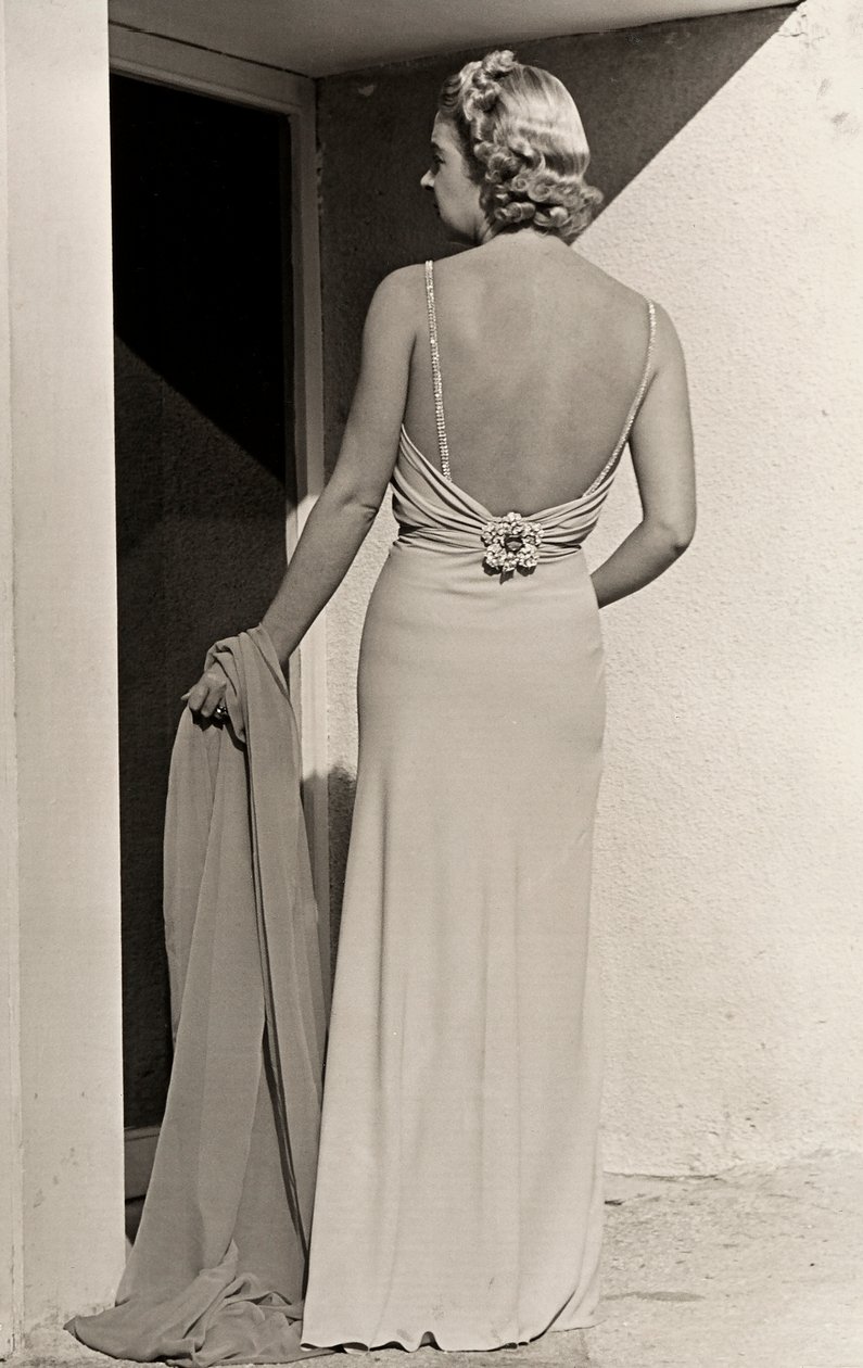 Modell von hinten gesehen trägt Abendkleid des Modehauses "Fumach". Der Artikel lässt den Rücken frei und ist mit einer juwelenbesetzten Brosche verziert. von Luis Bogino