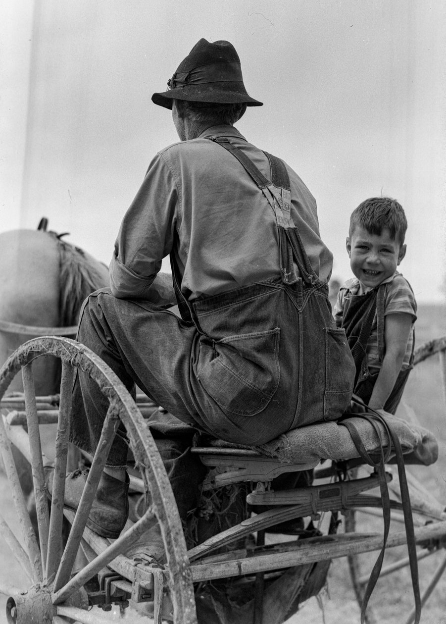Bauer und lächelnder Junge fahren auf dem Sitz eines pferdegezogenen Wagens in West Virginia von Volkmar Wentzel