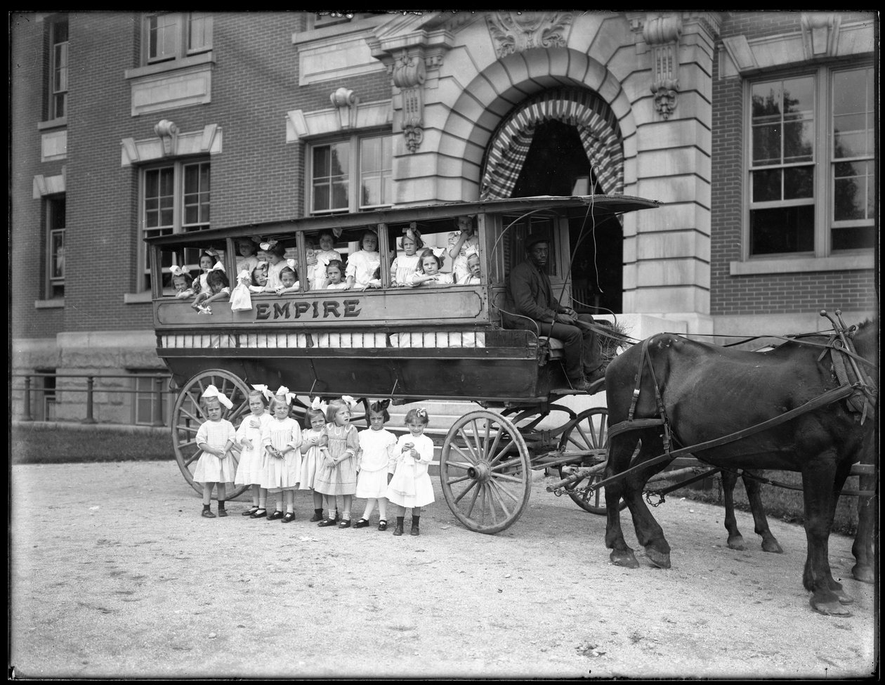 Kleine Mädchen posieren in und vor einem Pferdewagen, vor einem unbekannten Gebäude, wahrscheinlich das römisch-katholische Waisenhaus, Kingsbridge, Bronx, ca. 1910 von William Davis Hassler