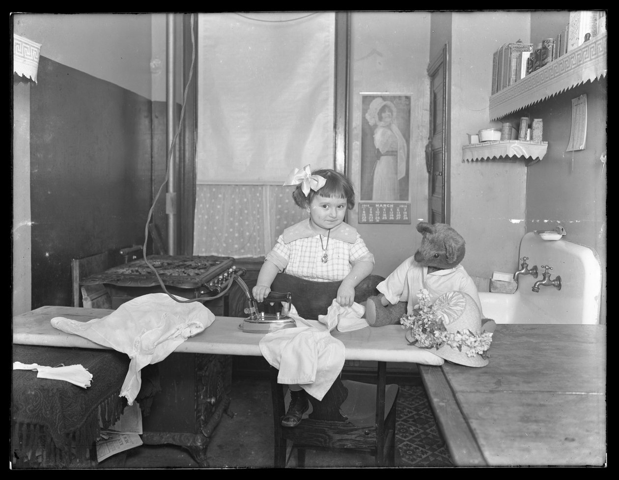 Unidentifiziertes kleines Mädchen, das die Verwendung eines elektrischen Bügeleisens demonstriert, c.1913-14 von William Davis Hassler