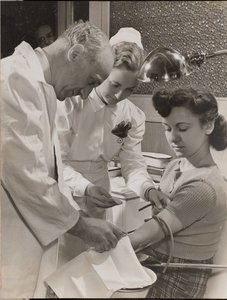 [Arzt und Krankenschwester setzen einer Frau eine Nadel ein] von Arnold Eagle