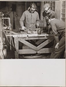 Drei Männer mit Schutzbrillen schweißen ein Metallstück auf einem Tisch