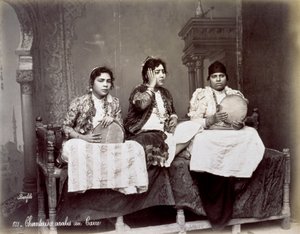 Porträt von drei jungen arabischen Sängerinnen in ethnischer Kleidung mit langen Halsketten. Sie posieren im Studio, sitzend. Zwei von ihnen halten ein Tamburin