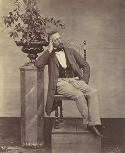 Mathias Höusermann, sitzend mit Ellbogen auf Sockel, hält eine Vase mit Blumen