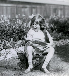 Ein junges Mädchen, Betty, hält eine östliche Indigo-Schlange, während sie auf einem Lederkoffer sitzt, Londoner Zoo, 1924 von Frederick William Bond