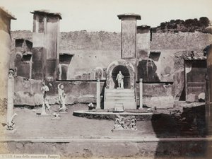 Teilansicht des erhöhten Gartens des Hauses des Marcus Lucretius in Pompeji, dekoriert mit Marmorstatuen und Hermen. In der Mitte ein Brunnen mit einer Nische. Im Hintergrund Fragmente von Wandmalereien von Giorgio Sommer