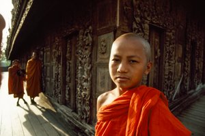 Ein junger Novizenmönch vor geschnitzten Teakholztafeln. Shwenandaw-Kloster, Mandalay, Burma.