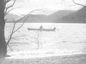 Ein Mann sitzt in einem Boot auf einem See und angelt, mit Hügeln im Hintergrund