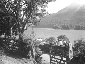Vier Personen sitzen auf einer Trockenmauer und machen ein Picknick mit Blick auf den See, Auto mit offenem Kofferraum geparkt von Joseph Hardman