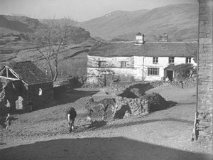 Drei junge Jungen beobachten Pferde im Bauernhof in Kentmere mit Bauernhaus und Hügeln dahinter von Joseph Hardman