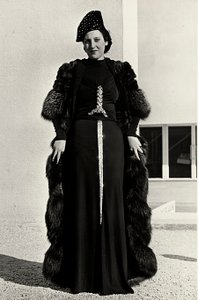 Modell im Abendkleid des italienischen Modehauses "Dragoni". Die Vorderseite des Artikels hat eine auffällige Paillettenverzierung in Form eines Schwertes. Ein Hut und ein Pelzmantel vervollständigen das Ensemble. von Luis Bogino