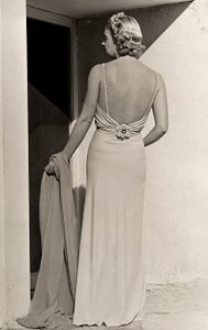 Modell von hinten gesehen trägt Abendkleid des Modehauses "Fumach". Der Artikel lässt den Rücken frei und ist mit einer juwelenbesetzten Brosche verziert. von Luis Bogino