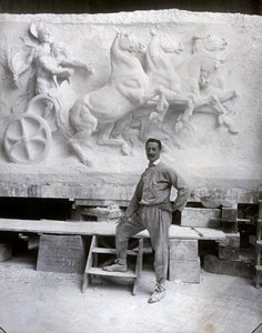 Ganzkörperporträt des berühmten Bildhauers Pietro Canonica. Er posiert in seinem Atelier vor einem Marmorhochrelief, an dem er arbeitet