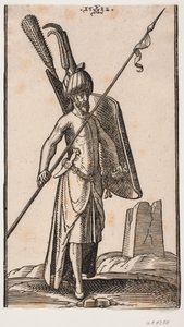 Stehender Soldat mit krummem Schild in der linken Hand und einem schräg gehaltenen Speer in der rechten Hand; Schwert an seiner linken Seite, ein Dolch im Gürtel an seiner linken Seite; im Hintergrund rechts die Ruine eines Obelisken oder eines Turms mit q