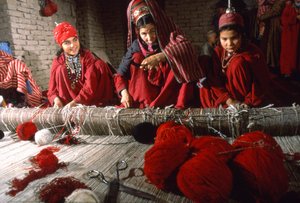 Turkmenische Stammesfrauen schneiden Knoten im Schuss eines Teppichs auf einem Webstuhl in einem Dorf