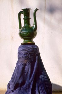 Frau in Kabul, abgeschirmt durch einen Seiden-Chadri alias Chador, trägt einen Krug