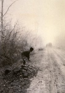 Eine Landstraße in Morgennebel gehüllt. Im Vordergrund spaltet ein Mann Steine von Unbekannter Künstler