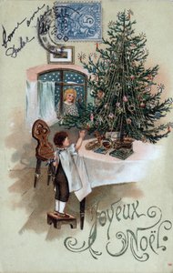 Weihnachtsgrußkarte: Ein Kind vor einem Weihnachtsbaum posiert auf einem Tisch, beobachtet von einem Engel im Fenster - Postkarte von 1905. von Unbekannt