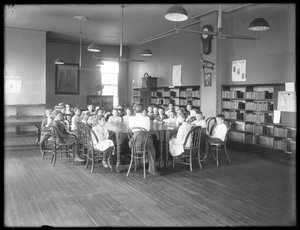 Kinder hören einer Frau im Lesesaal einer nicht identifizierten Filiale der Queens Borough Public Library zu, ca. 1910 von William Davis Hassler