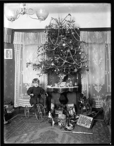 Seymour-Junge posiert sitzend auf Dreirad neben Weihnachtsbaum im Wohnzimmer, Weihnachten 1912 von William Davis Hassler