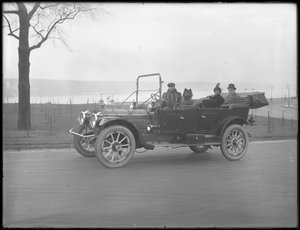 Drei nicht identifizierte Personen und zwei Chow-Hunde fahren in einem Cabriolet entlang eines Flusses oder Sees, ca. 1912 von William Davis Hassler