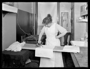 Unidentifizierte Frau, die die Verwendung eines elektrischen Bügeleisens demonstriert, ca. 1913-14