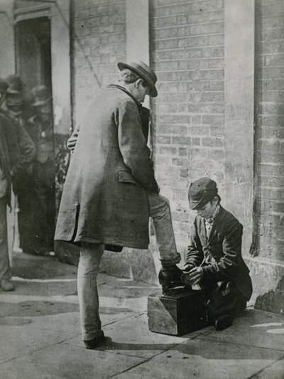Ein junger Schuhputzer putzt die Schuhe eines Mannes auf der Straße von English Photographer