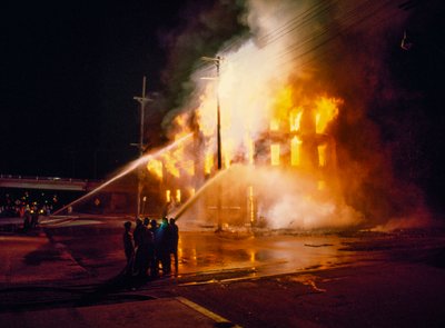 Ein städtisches Gebäude vollständig in Flammen in Kansas City bei Nacht mit Feuerwehrleuten von Ted Spiegel