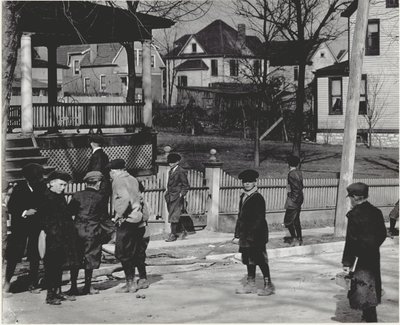 Eine Gruppe von Jungen in Wintermänteln steht auf einer unbekannten Straße entweder vor oder nach einem Schultag. von Unbekannt