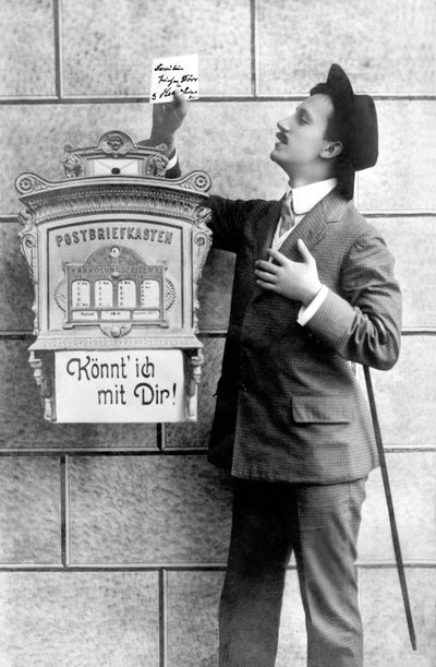 Ein eleganter Mann im Anzug, Hut und Stock, steckt eine Notiz in einen Briefkasten. Deutschland um 1920. Historische Fotografie, Mann neben einem Briefkasten, um 1920 von Unbekannt