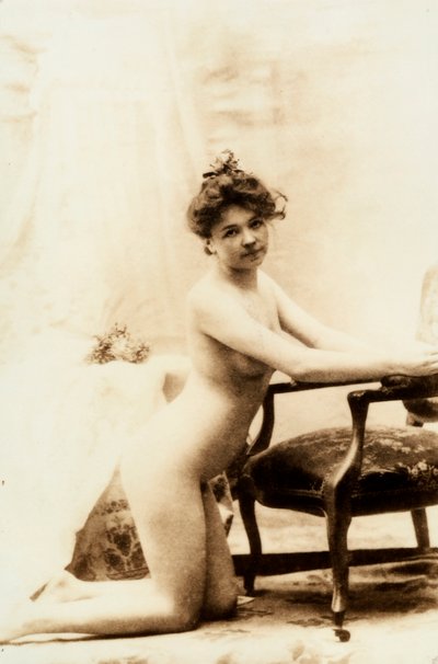 Nacktporträt einer jungen Frau, die vor einem kleinen Sessel kniet. von Unknown photographer