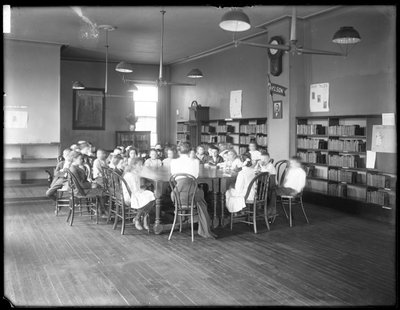 Kinder hören einer Frau im Lesesaal einer nicht identifizierten Filiale der Queens Borough Public Library zu, ca. 1910 von William Davis Hassler