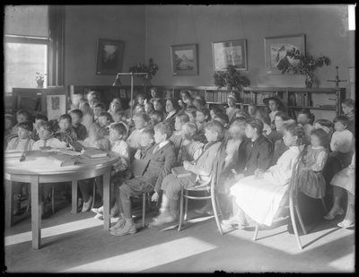 Kinder sitzen und hören im Lesesaal einer nicht identifizierten Filiale der Queens Borough Public Library, um 1910 von William Davis Hassler