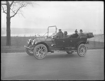 Drei nicht identifizierte Personen und zwei Chow-Hunde fahren in einem Cabriolet entlang eines Flusses oder Sees, ca. 1912 von William Davis Hassler