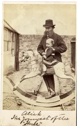 Junges Mädchen auf einem Schaukelpferd im Garten, ihr Vater daneben