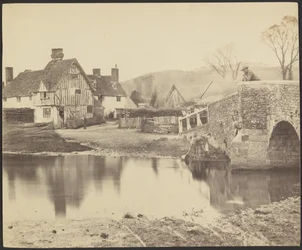 Ansicht eines Hauses über einen Fluss mit einer Brücke rechts
