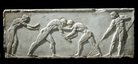 Griechische Kunst: Basis eines Kouros mit der Darstellung ringender Kämpfer während eines Kampfes. Marmorrelief mit Ringern, 510-500 v. Chr. - Athen, Archäologisches Museum - Kämpfende Ringer - Marmorrelief an einer Kouros-Skulptur, 510-500 v. Chr.