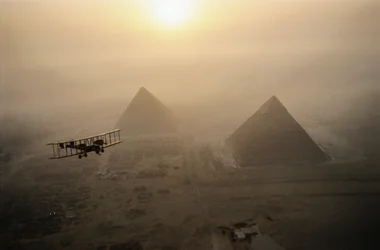Das Vintage-Flugzeug Vimy fliegt über nebelverhüllte Pyramiden während eines goldenen Sonnenaufgangs