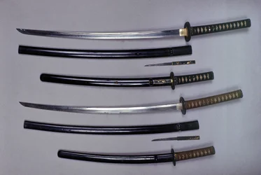 Oben: ein Katana, japanisches Schwert und seine Scheide, Wakizashi, japanisches Kurzschwert in seiner Scheide, kleiner Kokatawa-Dolch in derselben Scheide. Alle drei aus dem 18. Jahrhundert. Die unteren aus dem 17. Jahrhundert