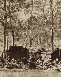 Australische Aborigines, die sich hinter einem Windschutz verstecken