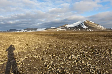 Schatten eines Menschen, polygonaler Strukturboden auf dem Plataberget, im Hintergrund der schneebedeckte Gipfel Nordenskjöldfjellet, nahe Longyearbyen, Spitzbergen, Svalbard, Norwegen, Europa