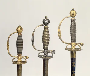 Griffe von drei französischen Schwertern: einer aus Stahl, gebläut und mit Goldgravuren verziert, um 1730; einer aus Stahl, durchbrochen und gemeißelt und der Grund aus mattiertem Gold, um 1760; einer aus gemeißeltem Stahl, gr