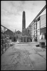 Allgemeine Ansicht des Elswick Shot Tower, abgerissen 1968-69, verwendet zur Herstellung von Bleischüssen, mit einem Hof mit Paletten im Vordergrund, ca. 1955-69